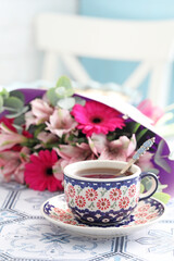 A beautiful ceramic cup and saucer with tea on a table. Flowers in the background. Selective focus.