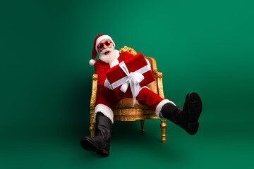 Santa Claus on a golden chair holding a present, with red sunglass against a vibrant green background