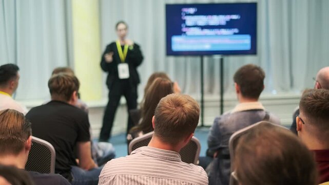Presenter conducting session for attendees in conference hall with screen displaying code topics