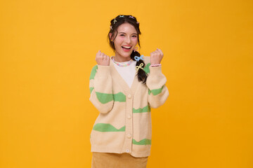 Smiling Asian woman with clenched fists in casual fashion outfit expressing excitement positivity confidence motivation and joyful lifestyle isolated on yellow background