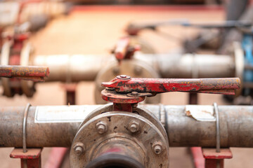 Handle controlling gate valve of water pumping unit which is used in oil field operation. Heavy industrial equipment object, close-up and selective focus at the valve handle.