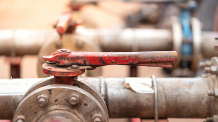 Handle controlling gate valve of water pumping unit which is used in oil field operation. Heavy industrial equipment object, close-up and selective focus at the valve handle.