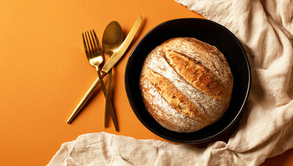 Black Bowl with Bread on Orange Background and Golden Cutlery