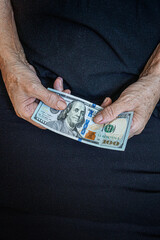 An elderly person holds one hundred dollars in his hand