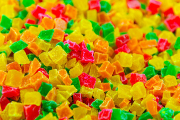 A close-up of a pile of candied fruit pieces. Sweet dried pineapple, orange, and papaya are used as fillings in confectionery and as an addition to breakfast muesli.