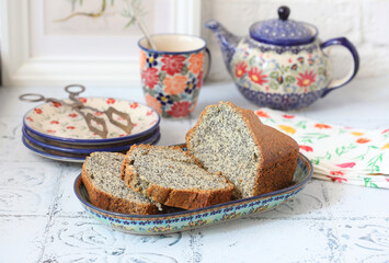 Homemade cake with poppy seeds on the table. Selective focus. A mug, saucer, and teapot in the background. 