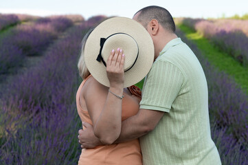 Couple embracing in lavender field, woman's face hidden by hat.