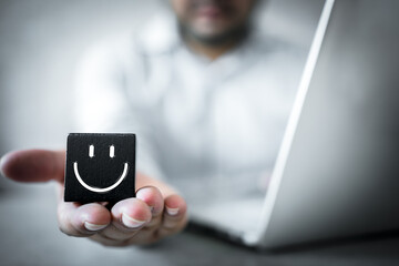 Wooden black block with happy face icons on man hand. Best rating for satisfaction present by giving rating