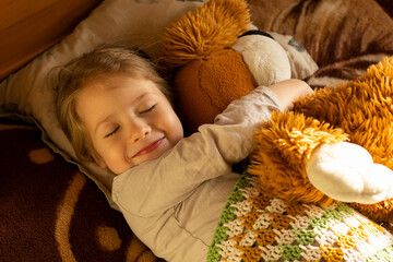 smiling little girl with closed eyes hugging her toy lying on the bed