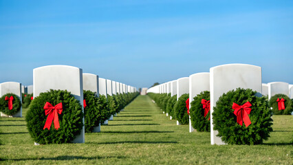 Rows of white headstones in a national cemetery adorned with green christmas wreaths and red bows on a sunny day