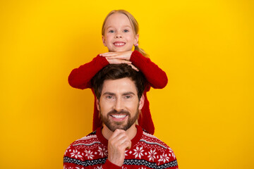 Happy father and daughter wearing red sweaters bonding together against a yellow background,...