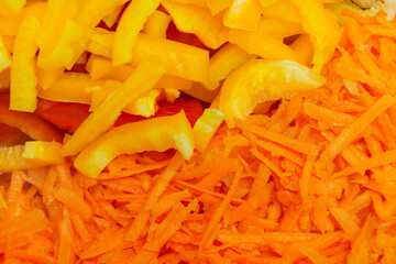 Freshly shredded carrots and sliced yellow bell peppers prepare for a colorful salad mix