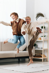 Two playful children jump mid air indoors, smiling and carefree as they wear cozy knitwear and...