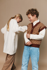 Two children share a playful moment in vintage style outfits, as a girl helps a boy adjust his...