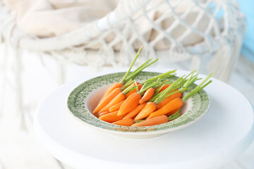 Young peeled raw carrots in a green plate on the summer porch. Selective focus.
