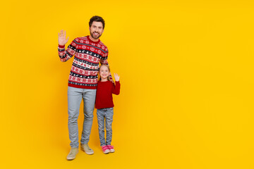 Fototapeta premium Father and daughter waving together joyfully in festive sweaters with a cheerful yellow background in a bright winter setting