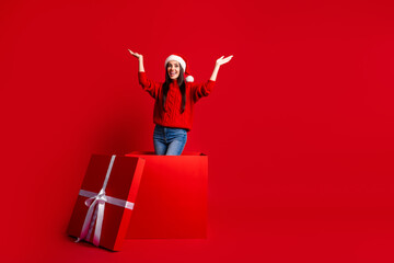 Excited young woman celebrates Christmas in festive Santa hat and cozy sweater, emerging from a...
