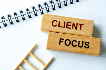 Client focus text written on a spiral notepad placed beside wooden blocks and ladder illustrating customer prioritization.