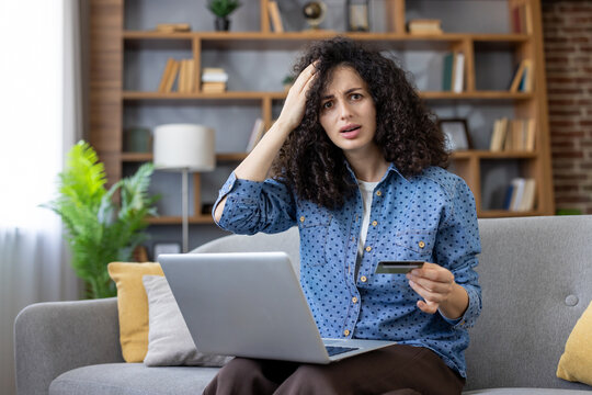 Young woman is having a payment issue while online shopping, holding a credit card and laptop, showing frustration and confusion with a failed transaction