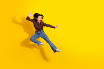 Obraz premium Young stylish woman jumping joyfully against bright yellow wall showcasing trendy autumn fashion in casual pullover