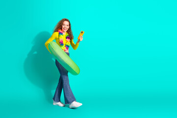 Energetic young woman in vibrant summer attire posing with a playful air, cheerful expression, and teal background
