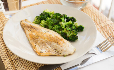 fried fillet of sea bass with garnish of broccoli on black warm stone plate