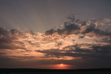 A picturesque sunset scene featuring a vibrant array of colors in the sky. The sun is setting on the horizon, casting a warm glow on the clouds and the land below.
