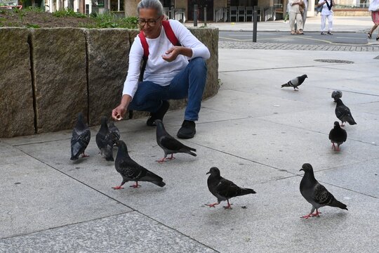 A smiling woman feeds pigeons on a busy city street. The scene conveys a sense of joy, spontaneity, and connection to nature in an urban setting.