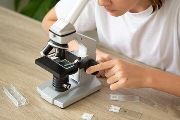 Girl studies biology at home while examining plants with a microscope during back-to-school season