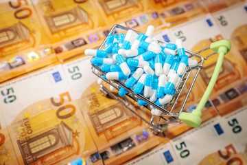 A small shopping cart filled with blue and white capsules placed on 50 euro banknotes, symbolizing pharmaceutical trade, drug costs, and healthcare economics.