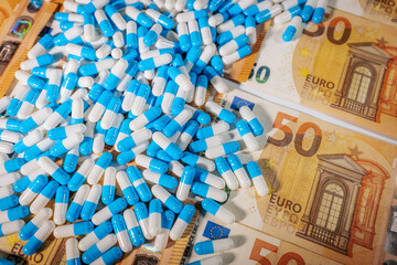 Blue and white capsules scattered over 50 euro banknotes, symbolizing pharmaceutical costs, healthcare expenses, medical economy, and drug industry.