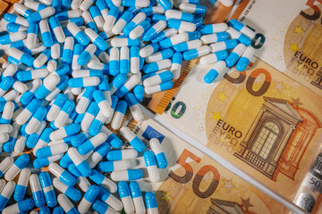Blue and white capsules scattered over 50 euro banknotes, symbolizing pharmaceutical costs,...