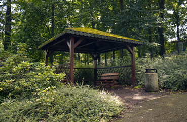 Wooden gazebo in the park under the trees. Gazebo with a sloping roof covered with green moss. A place for relaxation and sitting in the park.