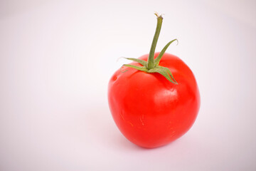 A vibrant red tomato with a green stem against a white background.