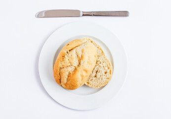 Bread roll on a plate with a knife, a simple breakfast scene.
