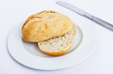 Freshly baked bread roll on a white plate with a knife, ready to be enjoyed.