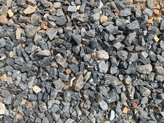 A high-angle, detailed shot of a dense pile of crushed gray stone and rock, with some hints of brown and red dirt, suitable for a construction or natural background.