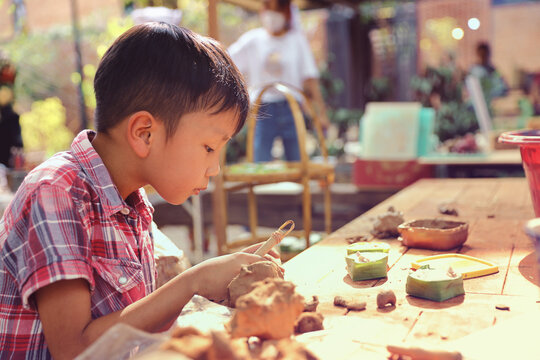 An Asian boy is learning about clay spinning and art to enhance his creativity. Young Boy Learning Pottery.