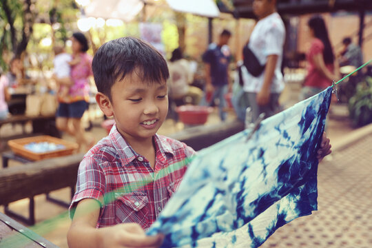 An Asian boy admires his tie-dye creation. Proud Boy with His Tie-Dye Creation.