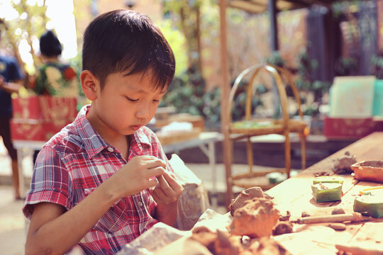 An Asian boy is learning about clay spinning and art to enhance his creativity. Young Boy Learning Pottery.