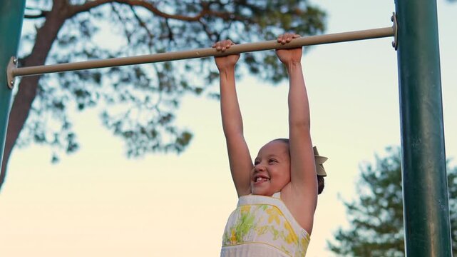 ni&ntilde;a divertida y feliz colgada de un pasamanos en un parque al aire libre entre los arboles jugando y disfrutando de su infancia e inocencia en un atardecer actividad fisica de ni&ntilde;os