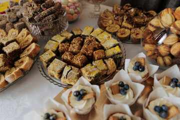 Wedding dessert table with a variety of sweets: cakes, muffins, jelly, rolls, cookies, and macarons. Bright and appetizing arrangement creating a festive atmosphere.
