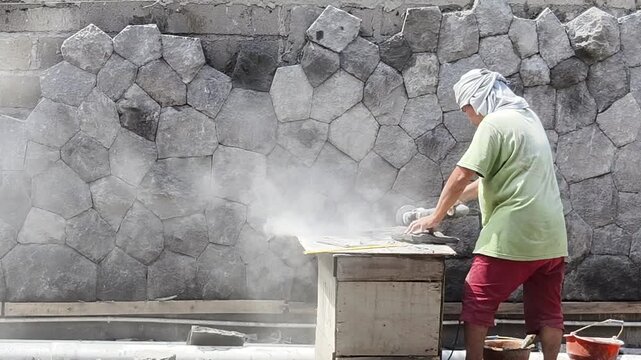 Badung, Bali, Indonesia &ndash; September 19, 2025: A local construction worker crafting and cladding a stone wall using an angle grinder with a diamond blade
