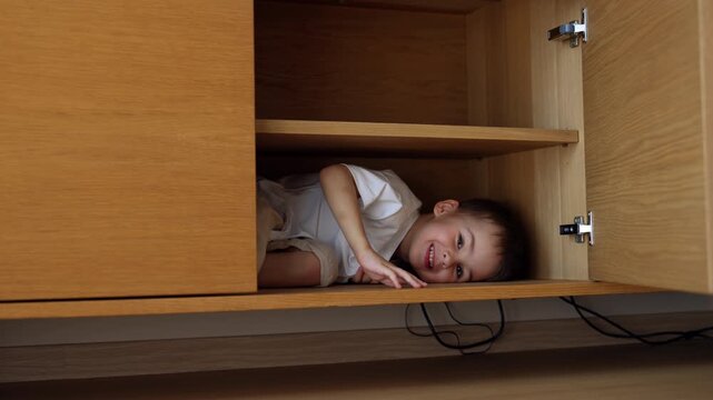Door of commode opens and a little kid hiding inside appears. Playful toddler smiles to camera.