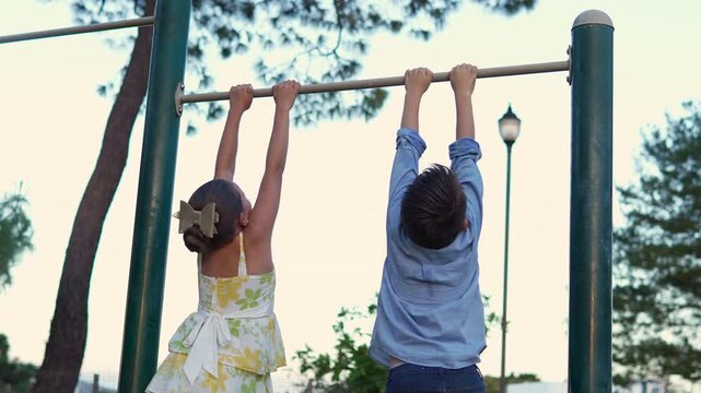 dos ni&ntilde;os felices divertidos colgados de un pasamanos disfrutando de su ni&ntilde;ez o infancia en un parque al aire libre con alegria y felicidad el ni&ntilde;o se cae al final