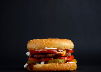 Close-up of a juicy burger with beef patty, fresh tomato slices, pickles, sauce, and sesame bun on dark background. Perfect fast food concept and street meal detail.