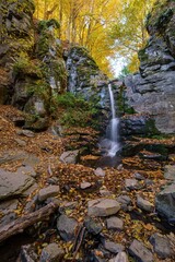 Scenic autumn waterfall flowing through rocky canyon surrounded by vibrant yellow and orange forest in the fall season. Peaceful nature scene full of color and texture.