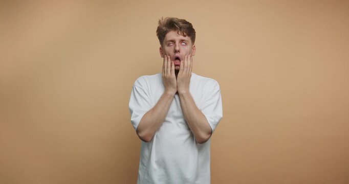 footage of young man shows a shocked expression, hands on face, illustrating a moment of surprise or realization on beige background