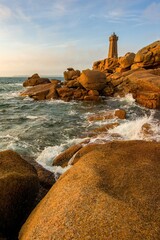 Scenic view of the Ploumanac'h lighthouse on the Pink Granite Coast in Brittany, France. Waves crash on the unique reddish rocks during golden hour. Famous travel destination in Europe.