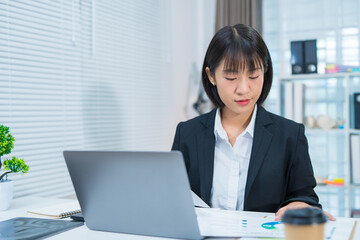 Asian businesswoman doing financial market research using laptop and digital tablet on digital investment in front of modern office.